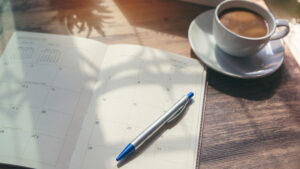 A planner, pen and coffee on a desk.
