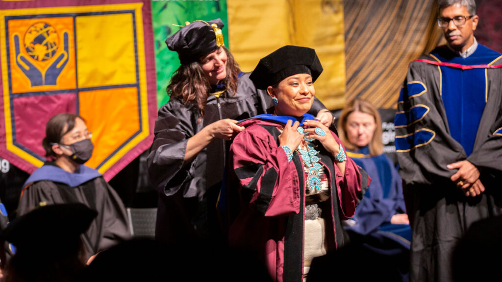 A doctoral graduate is hooded by her advisor.