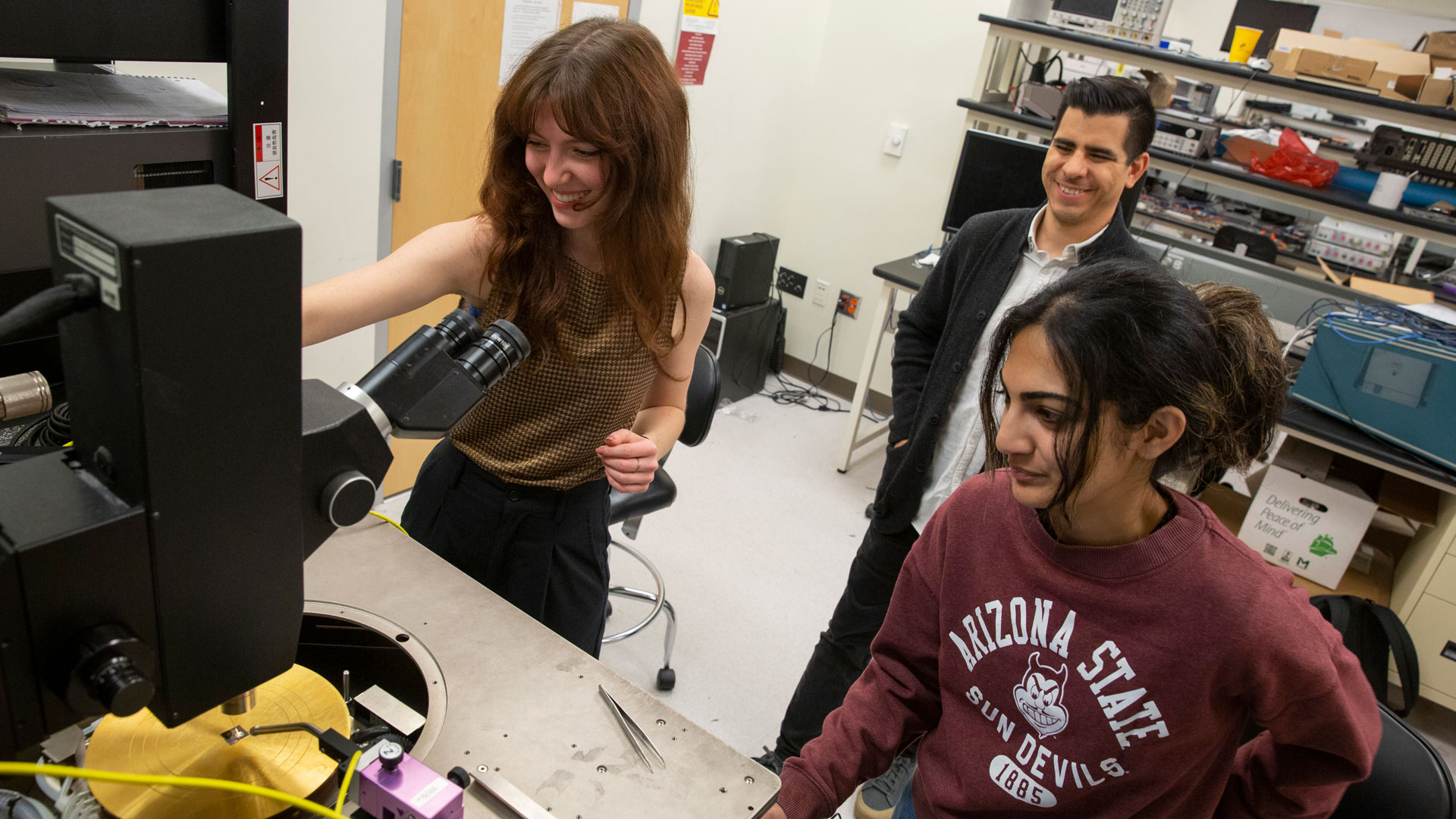 Two students work with lab equipment while their faculty mentor watches.