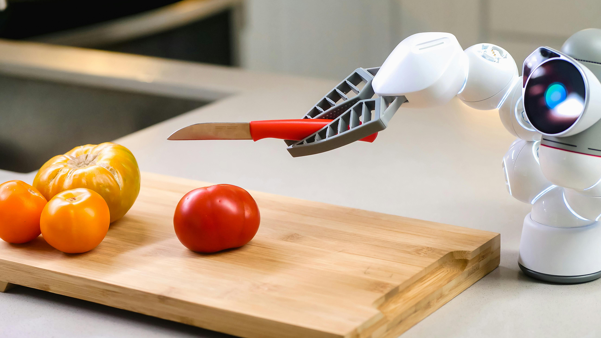 A small robot wields a knife and attempts to chop a red tomato
