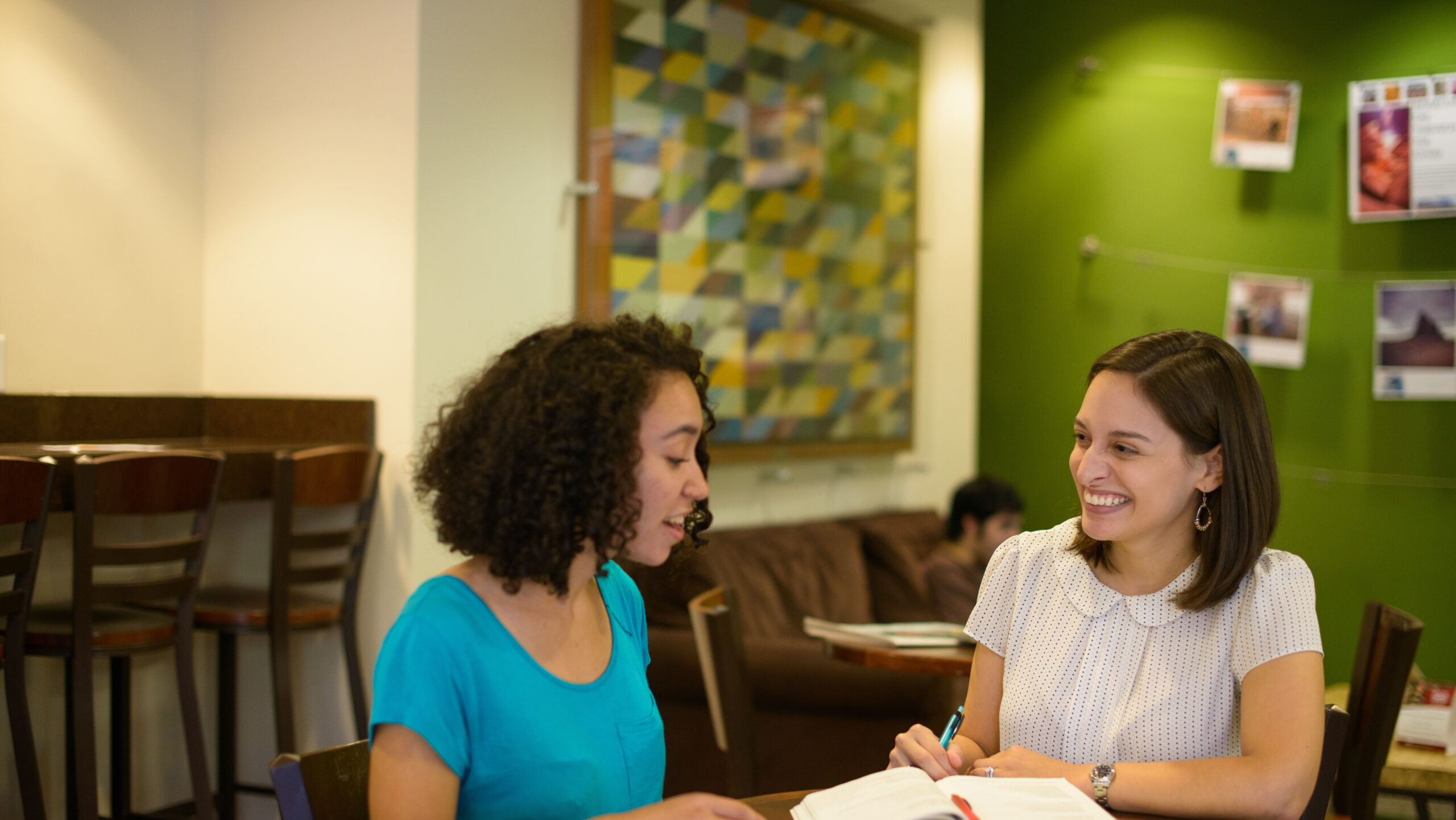 Two women look at a book while seated at a table