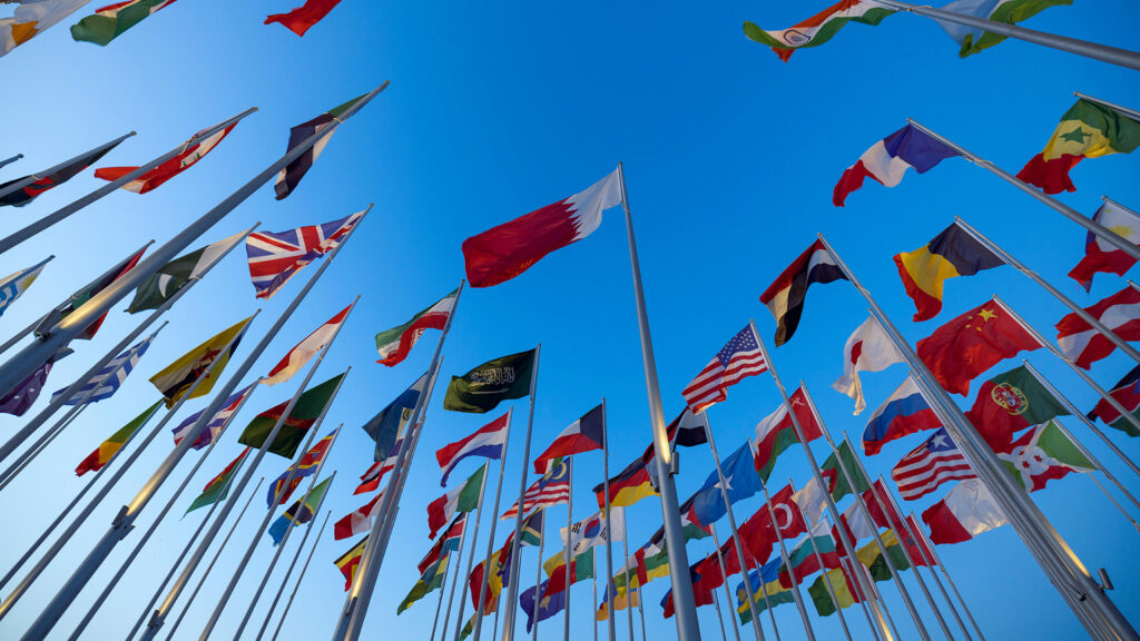 An array of international flags against a bright blue sky.